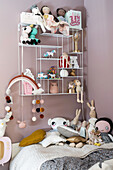 Wall shelf with dolls and decorative objects above a bed with cuddly toys