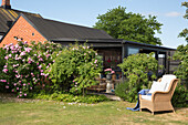 Korbsessel im sonnigen Garten, im Hintergrund überdachte Terrasse