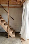 Wooden staircase in room with floor screed, white billowing curtain in front of window