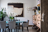 Oval table with upholstered chairs, modern art, and large wooden sideboard in a dining room
