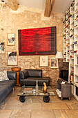 Sitzbereich mit Ledergarnitur und Regalwand im Wohnraum, moderne Kunst an Natursteinwand