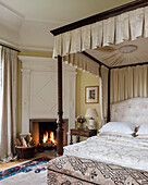 Bench upholstered with kilim at the end of a four poster bed in the bedroom with paneled fireplace wall