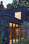 A Modern home with a zinc exterior and large windows at dusk