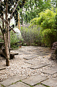 Garden square with gravel and concrete slabs, mountain bamboo at the fence