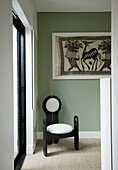 Designer chair above vintage artwork in a corner of a room with green wall