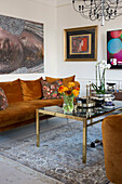rust colored plush sofa with cushions, artwork above and coffee table with glass top in bright living room