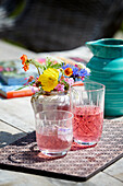 Rhubarb juice and colorful bouquet of flowers on an outdoor table