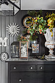 Black dresser with decorative objects and urn vase in front of grey wood paneled wall