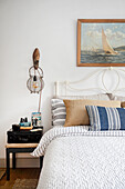 Queen bed with wrought iron headboard under a vintage sailboat painting