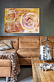 Moderne Kunst an dunkler Wand über hellbraune Sofagarnitur, Vintage Holztisch im Vordergrund