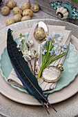 Place setting decorated with striped squill (Puschkinia scilloides), quail egg, silver spoon and feathers
