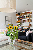 Glass coffee table with bouquet of flowers, armchair, and open wall shelf in the background