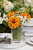 Vase of coneflowers (rudbeckia) and white tansy (Achillea ptarmica) on tray with cutlery