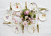 Plates with floral motif, gold-coloured cutlery and bouquet of flowers on a festively laid table