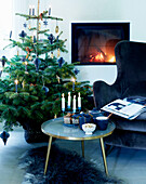 Coffee table with candles, blue velvet armchair and Christmas tree in front of fireplace