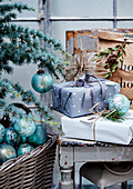 Weihnachtsgeschenke auf Holzstuhl und Korb mit türkisfarbenen Weihnachtskugeln unter dem Baum