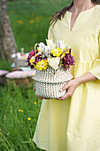 Woven basket with spring flowers in the hands of a woman in the garden