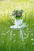Stool with wildflower bouquet of comfrey, goutweed, red clover (Trifolium pratense) and meadow sage in an old teapot