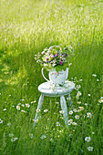 Hocker mit Wildblumenstrauß in alter Teekanne auf der Wiese, Beinwell, Giersch, Rotklee, Gänseblümchen und Wiesensalbei