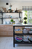 Black kitchen island workbench with marble top and crockery, in the background base units and wall shelf in the kitchen