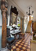 Carved wooden column, console table with chairs and wall mirror in eclectic hallway with tiled floor