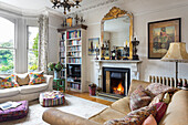 Mirror with gilded frame on mantelpiece, bookcase and sofas in living room with stucco ceiling