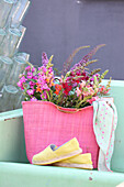 Gartenblumen in pinkfarbene Tasche auf Metallbank
