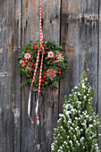 Christmas door wreath made of fir greenery, cones and red berries in front of a rustic wooden wall