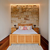 A wooden double bed in a bedroom with a sandstone wall
