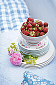 Frische Erdbeeren in einer Schale auf Tellerstapel mit Rosen dekoriert