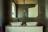 A washstand with two countertop sinks and mirrors in a bathroom with marble tiles