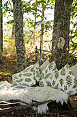 Old iron bed with pillows and sheepskin under treetops
