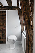 Toilette in hellgrauem Bad mit rustikalen Holzbalken