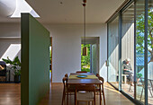 Essbereich vor Terrassentür aus Glas in offenem Wohnraum mit grün gestrichenem Raumteiler, Frau im Hintergrund