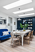 Long dining table with chairs and blue sofa in the dining area with skylight