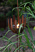 Rostiger Kerzenhalter mit brennender Kerze im Garten