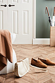 Stool with shawl, shoulder bag and loafers on parquet floor, in the background white double door and umbrella stand