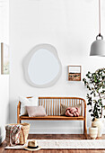Cushions on oak bench, wall mirror, house plant and pendant lamp in the hallway