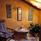 Bemalte Holzfensterläden an rauer Steinwand im spanischen Cottage-Wohnzimmer mit blauem Segeltuchstuhl und Zuckerrohrtisch