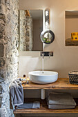 Wooden counter with vessel sink next to natural stone wall in an ensuite bathroom