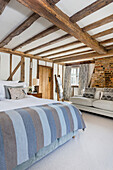 King size bed and sofa in light blue and grey tones in the bedroom with wood-beamed ceiling