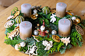 Advent wreath made out of mixed fir and conifer branches decorated with natural ornaments, wooden ornaments, and tin figures and golden white candles