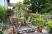A wooden terrace with garden chairs and a table and summer flowers in hanging basket