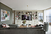 Grey sofa set, large-format painting on the wall and shelf unit in the living room with floor-to-ceiling glazing