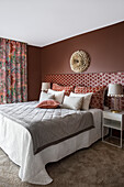 Double bed with high headboard and matching pillows in the bedroom in warm red tones