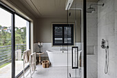 Shower area with mirrors and free-standing bathtub in spacious bathroom with balcony