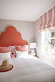 Double bed with generous, coral-colored headboard, flanked by bedside tables with white lamps