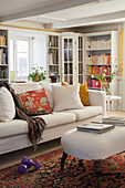 Comfortable sofa, antique French stool as coffee table, bookshelf in the background