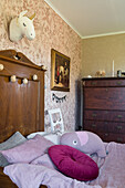 Antique wooden bed with high headboard in room with wallpapered wall