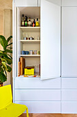 White, built-in kitchen cabinet with open door, yellow chair in front of it